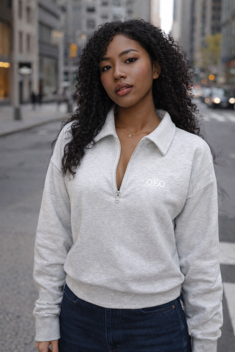 Woman wearing a gray sweatshirt with a logo on a city street